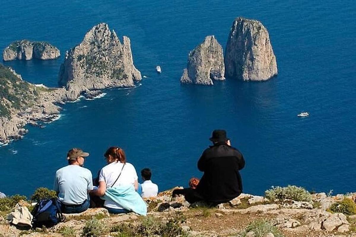 група людей, що сидять на вершині пагорба та дивляться на океан