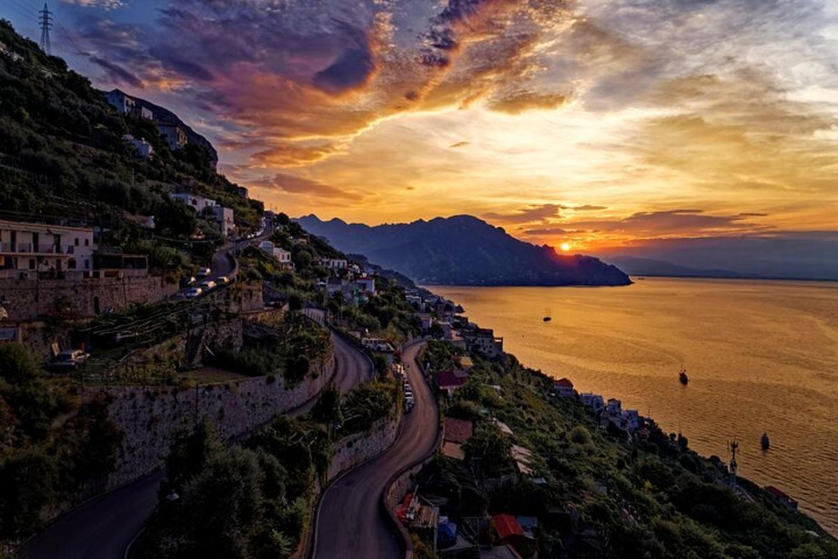 a sunset on a hill with a road next to the water