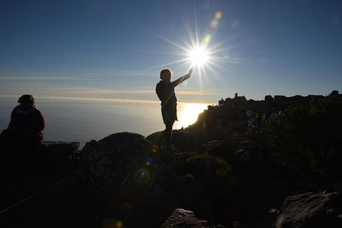 osoba stojící na skále se sluncem na obloze