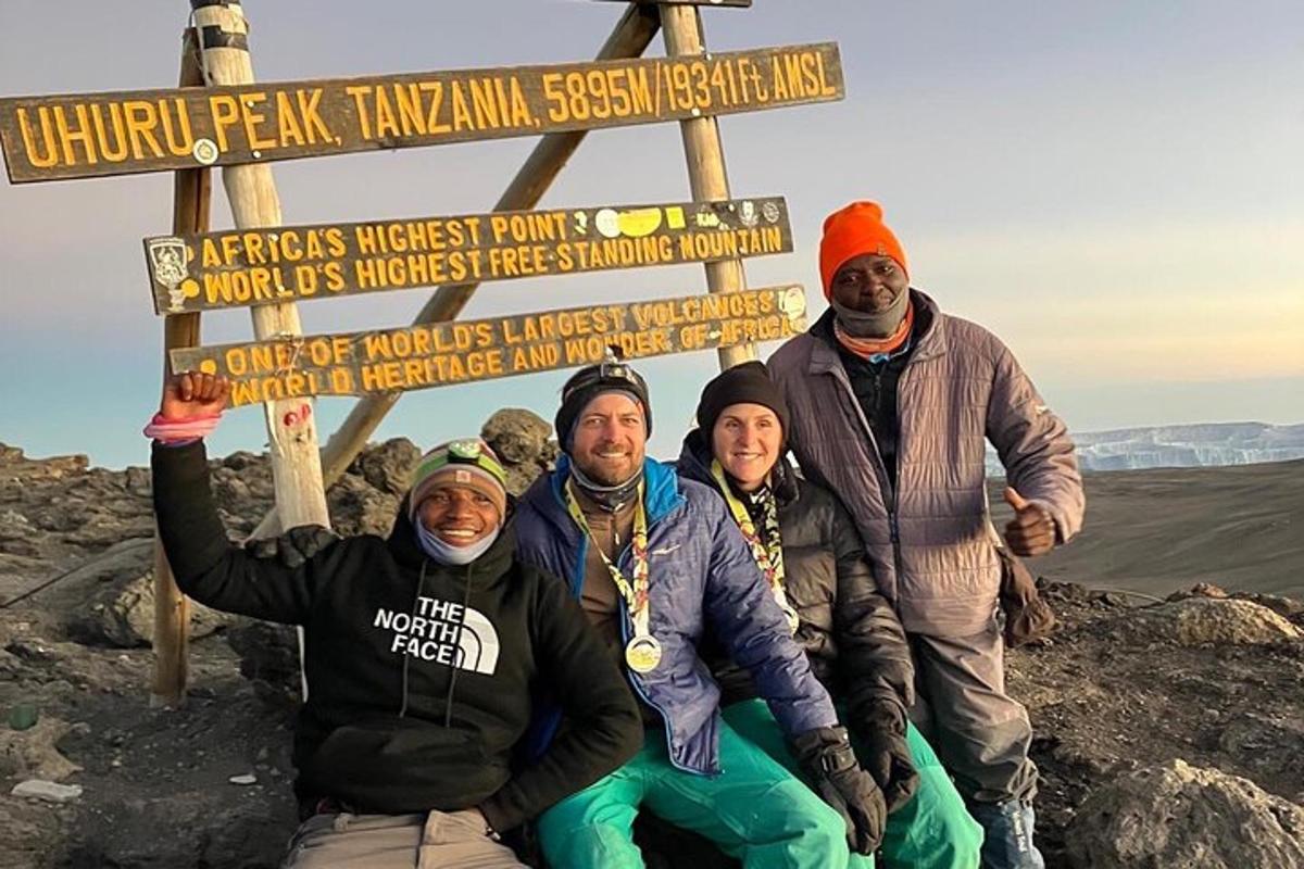 sekumpulan orang berdiri di sebelah papan tanda di atas gunung