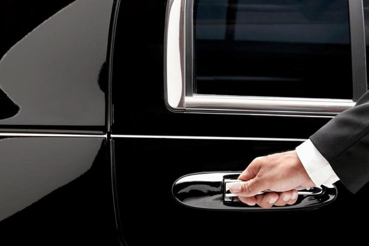 ülikonnas mees hoiab auto ukselingist kinni