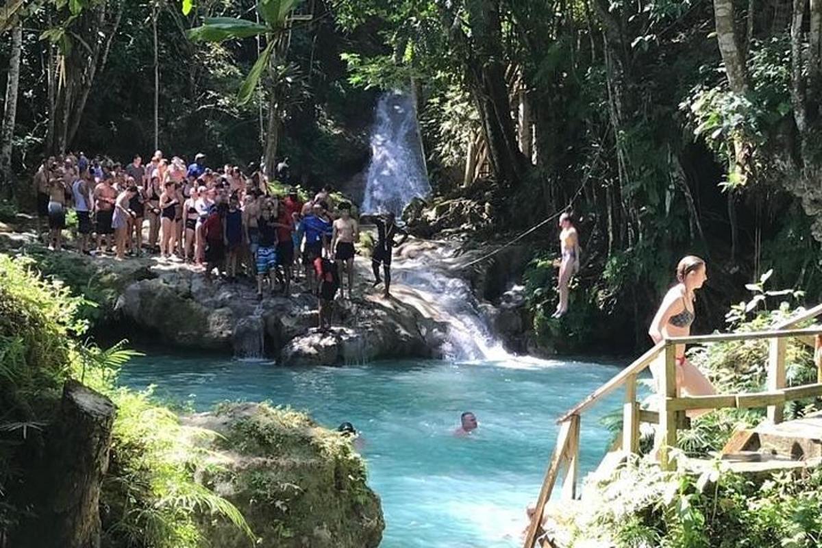 sekumpulan orang berdiri di kolam di hadapan air terjun