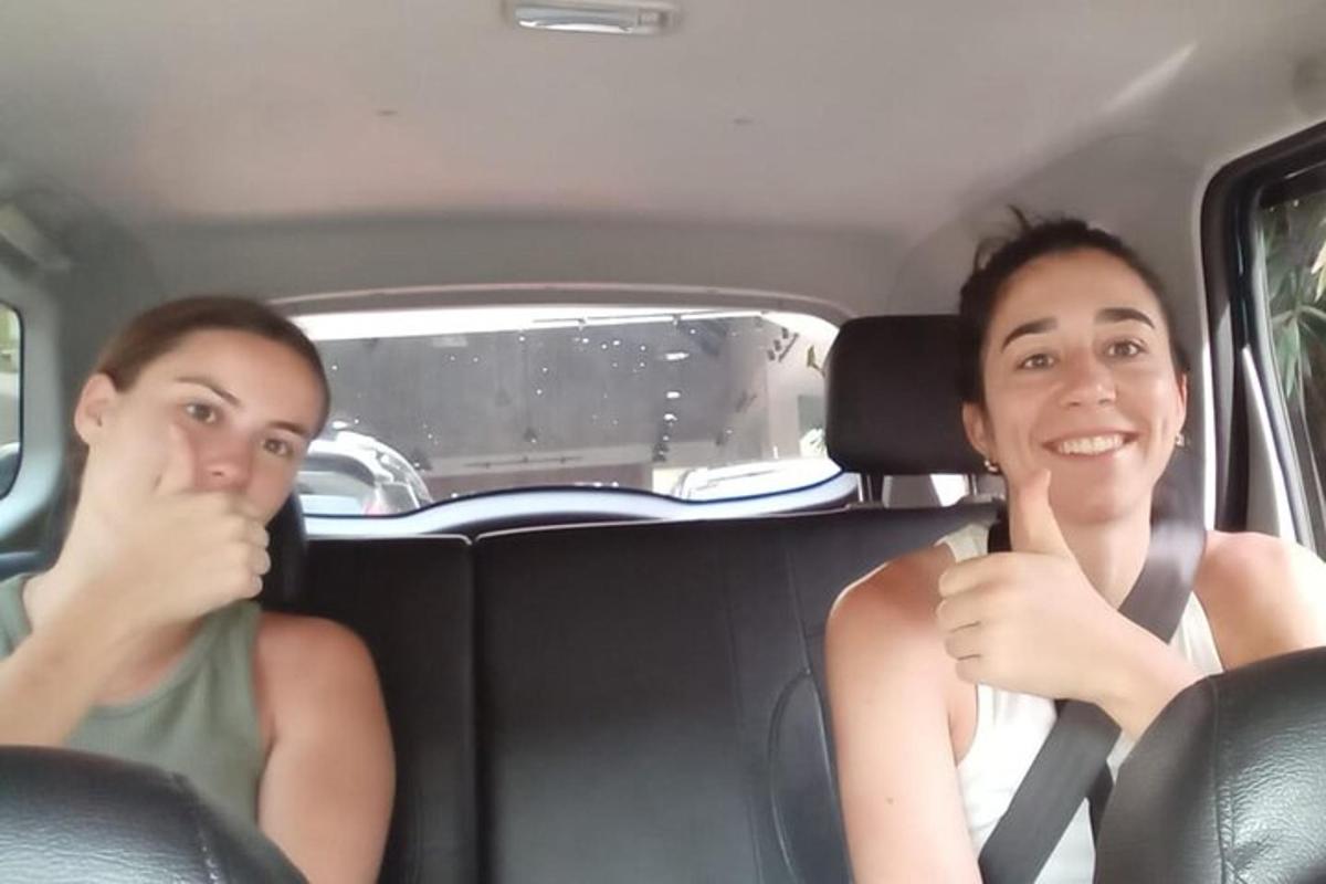 duas mulheres sentadas em um carro fazendo sinal de positivo