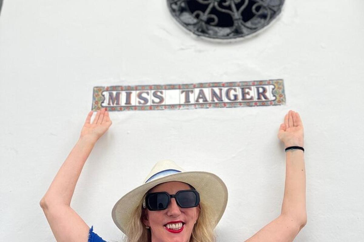 en kvinne med hatt og solbriller som holder et «miss ranger»-skilt på en vegg