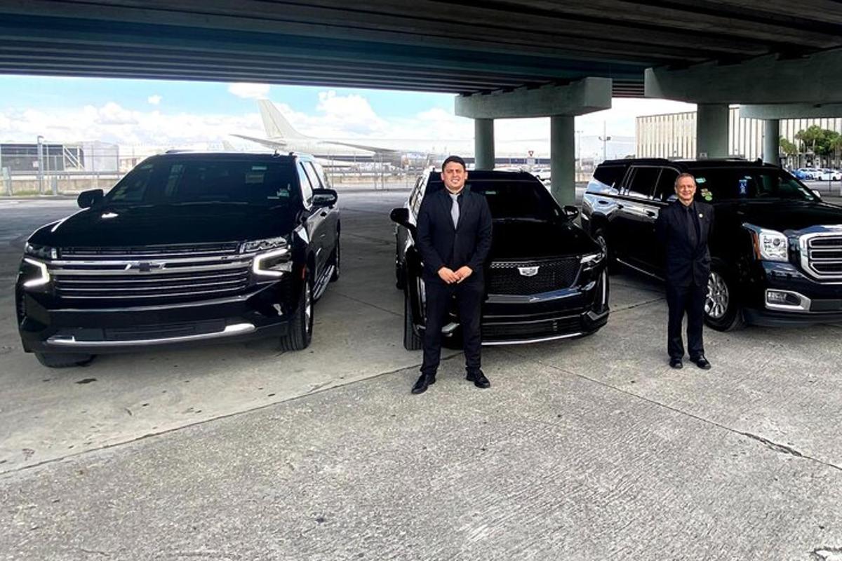 dois homens de terno parados ao lado de dois veículos de luxo