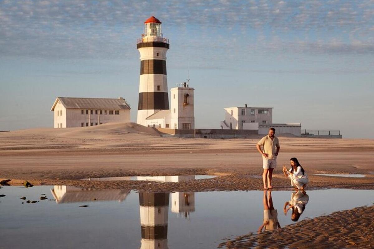 a man and a woman standing on the beach with a lighthouse