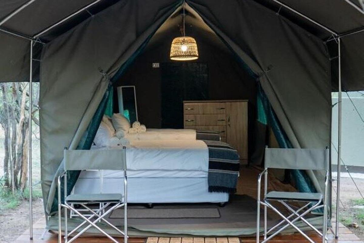 Una tienda de campaña con una cama y dos sillas dentro.