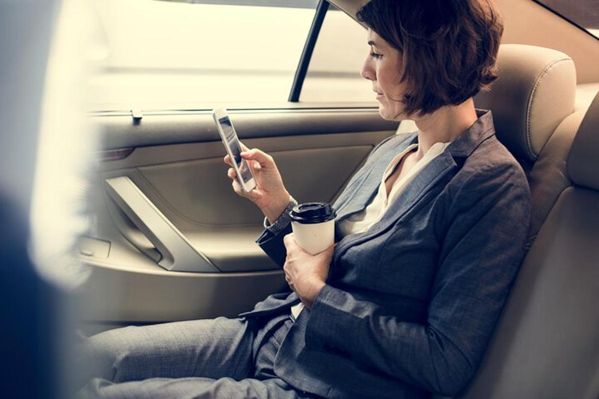 egy nő ül egy autó hátsó ülésén, és a mobiltelefonját nézi