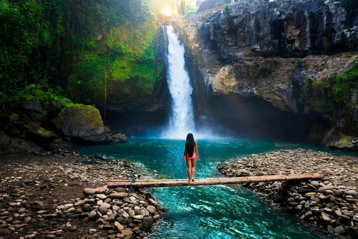a woman standing on a log in front of a waterfall