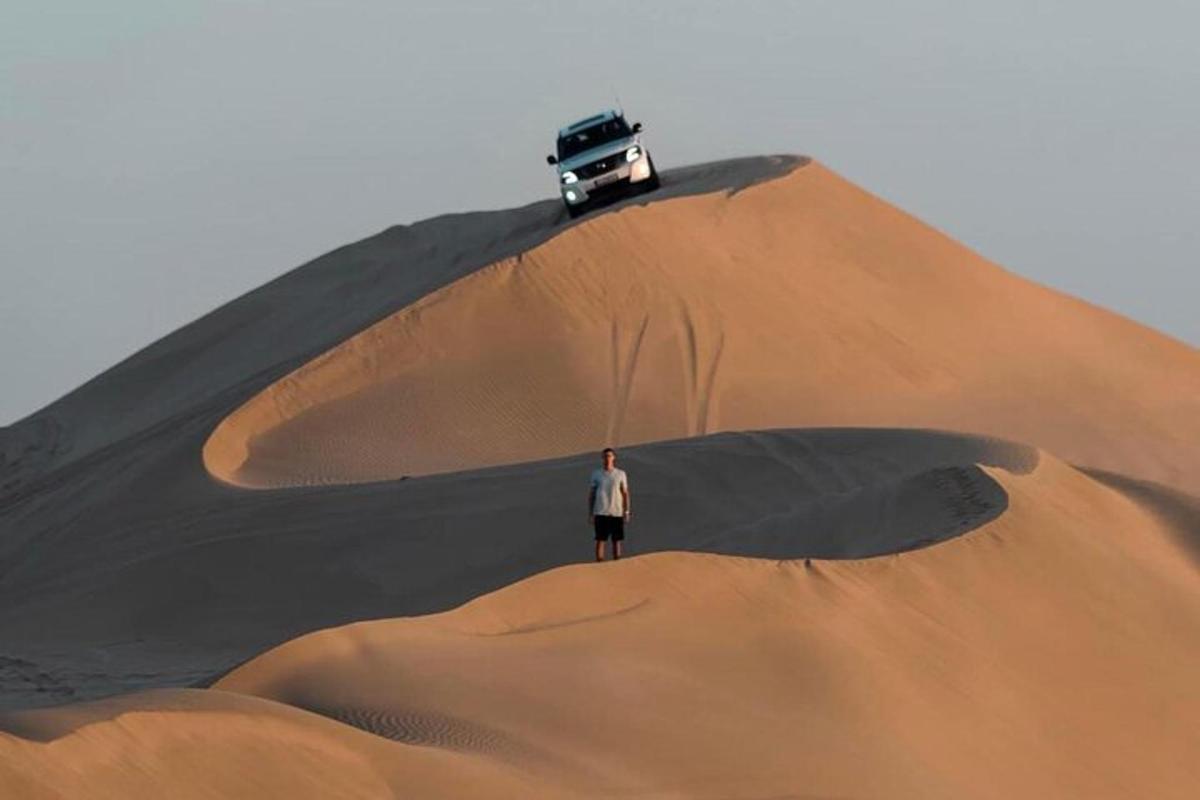 a man standing on a sand mound with a car on top