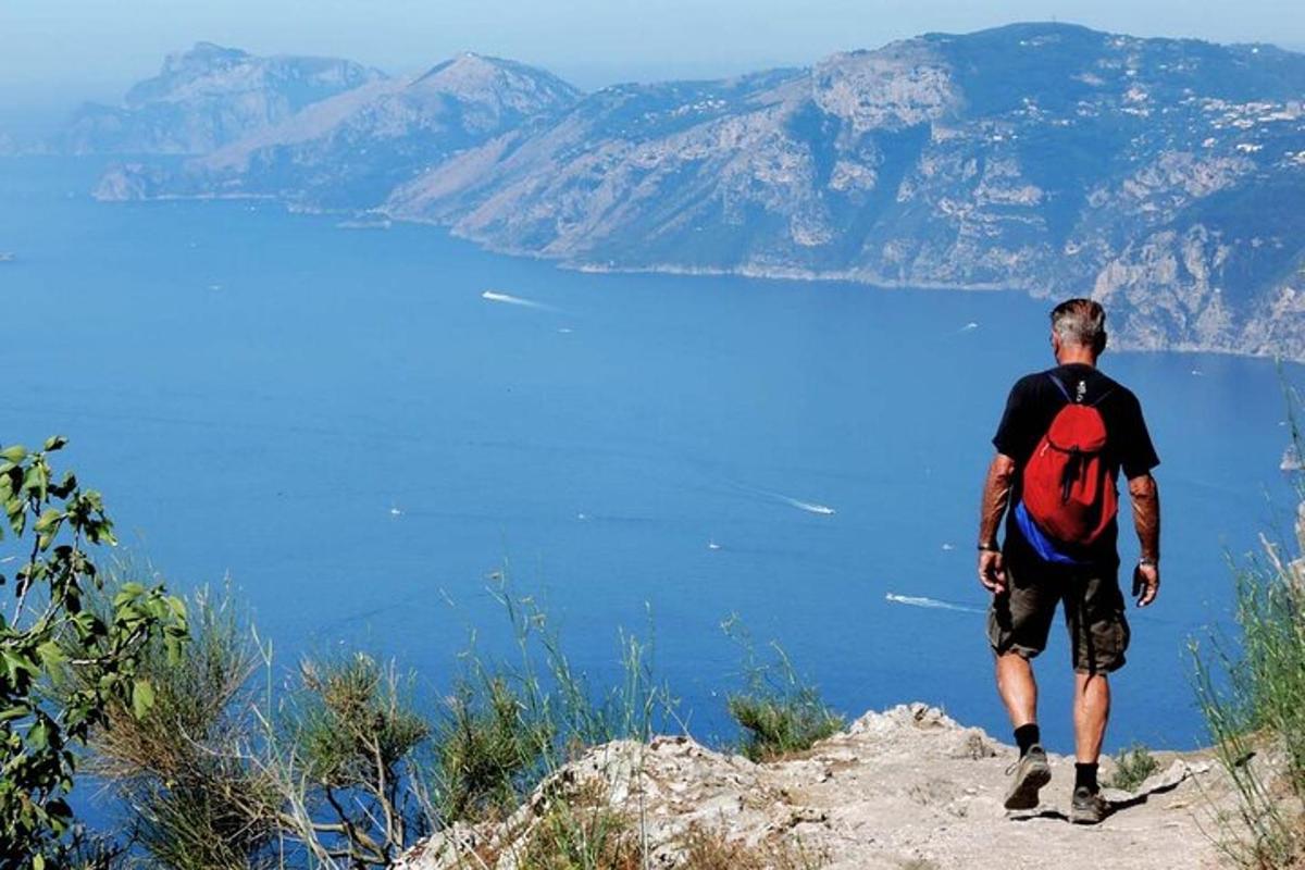 muž s batohem stojící na vrcholu hory