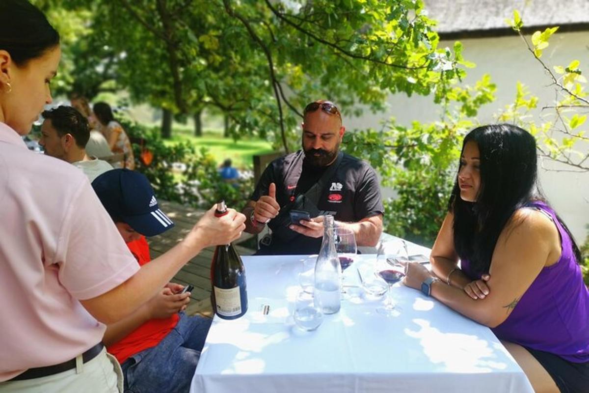 skupina lidí sedících kolem stolu s lahví vína