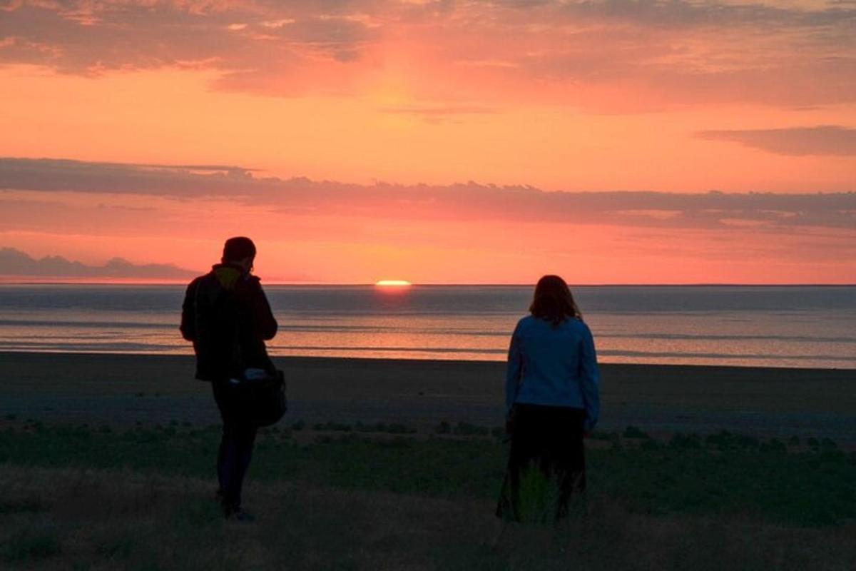 two people standing on the beach watching the sunset