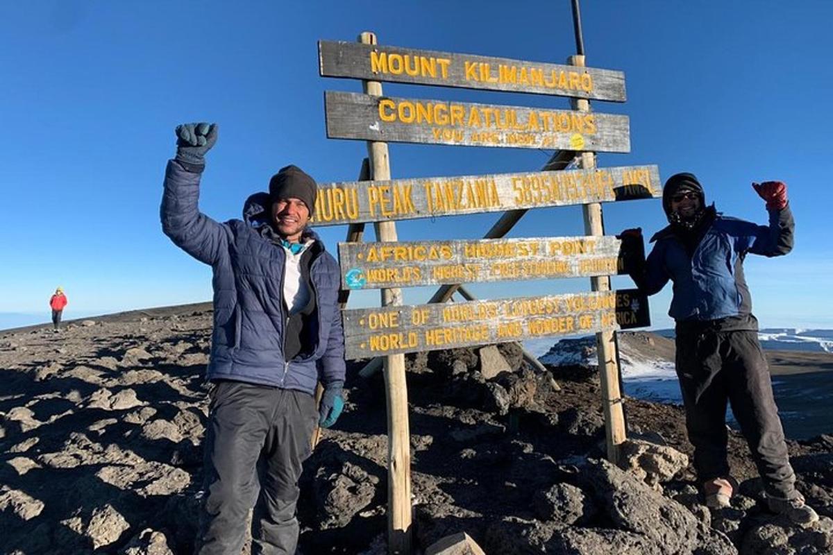 due uomini in piedi accanto a un cartello in cima a una montagna