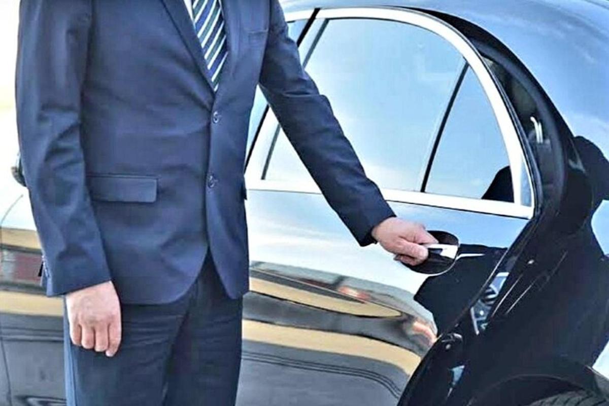 Ένας άντρας με κοστούμι στέκεται μπροστά από ένα αυτοκίνητο