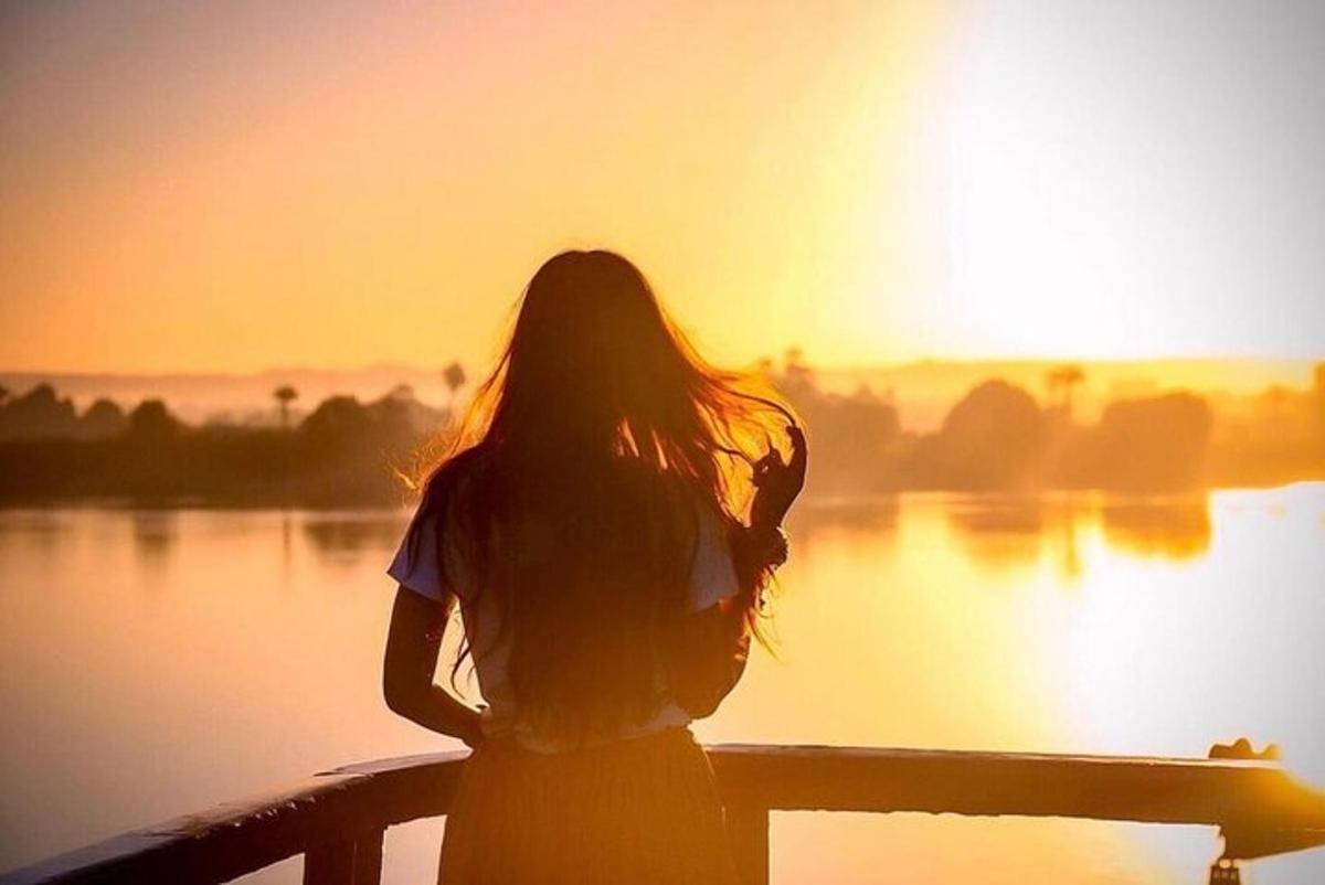 a woman standing in front of a lake at sunset
