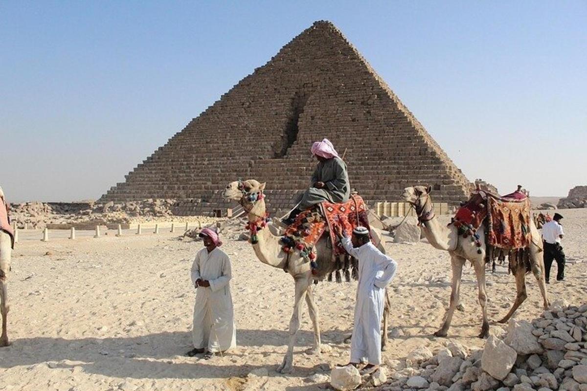 en gruppe mennesker som rir på kameler foran en pyramide