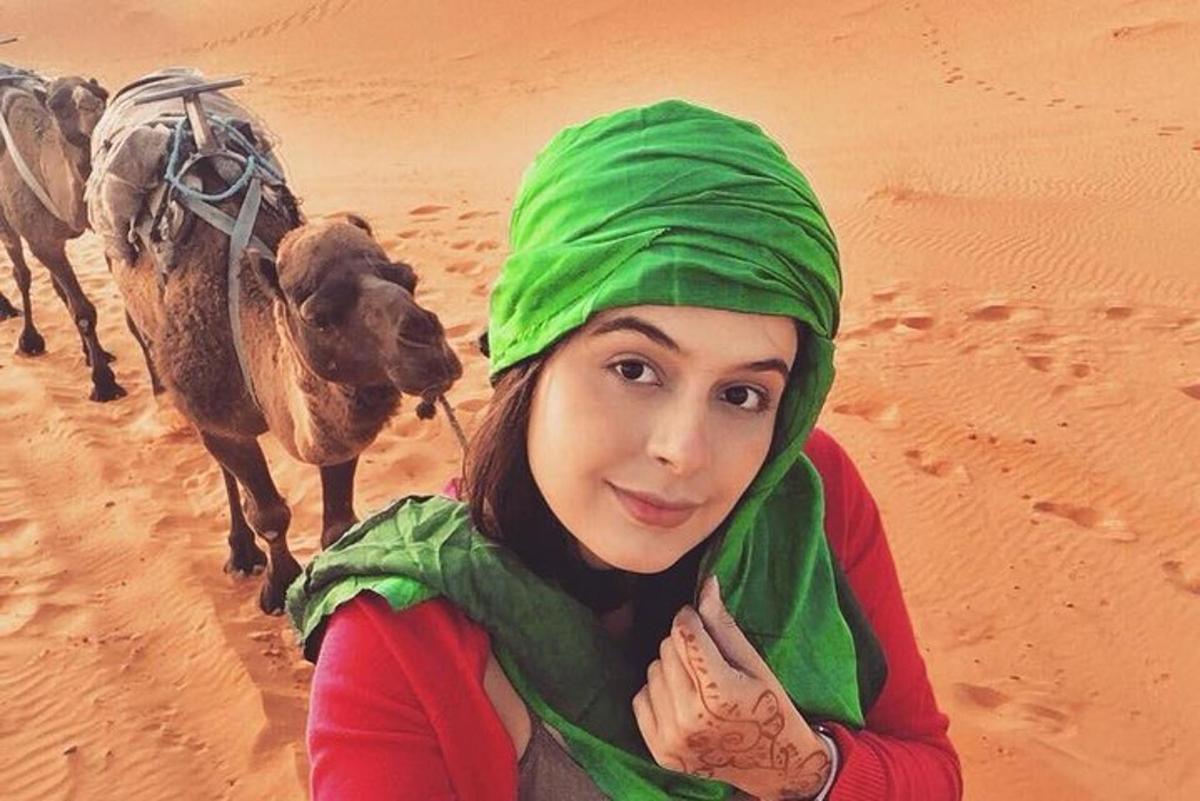 eine Frau in einem grünen Hijab steht mit Kamelen in der Wüste