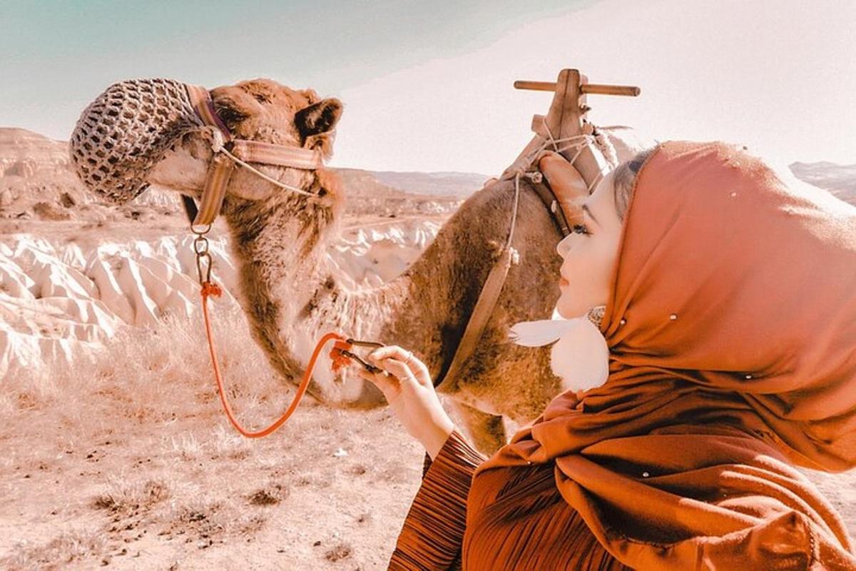 uma mulher sentada ao lado de um camelo no deserto