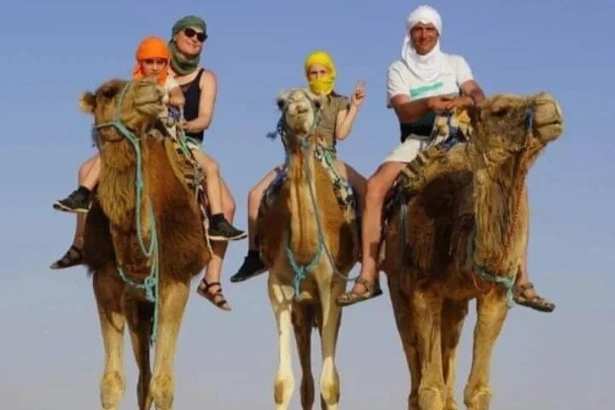 a group of four people riding on the backs of camels