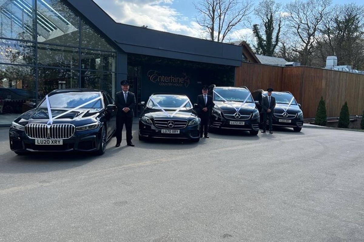 a group of people standing next to three luxury cars