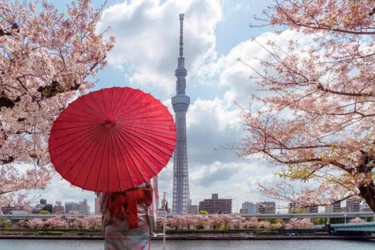 uma pessoa segurando um guarda-chuva vermelho em frente à torre de Tóquio