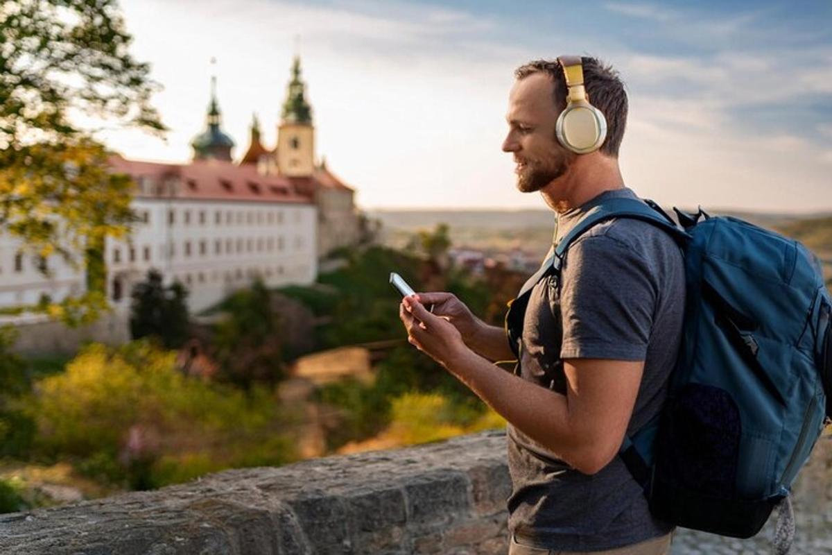 un bărbat cu căști și un rucsac care se uită la telefonul său mobil