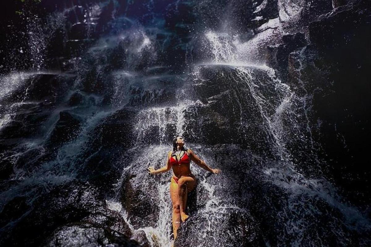 eine Frau sitzt auf einem Felsen vor einem Wasserfall