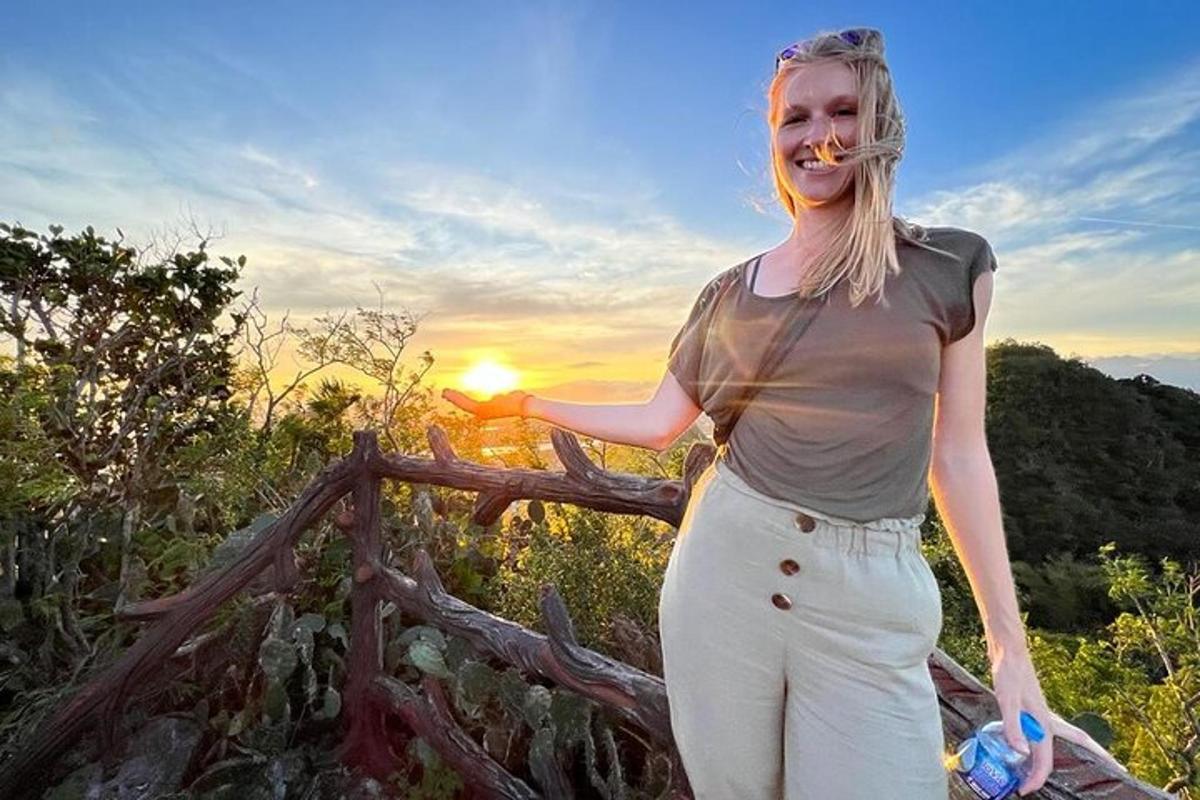 uma mulher parada ao lado de uma cerca com o pôr do sol ao fundo