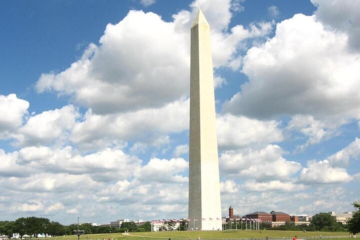 un alto obelisco bianco in un campo con un cielo nuvoloso