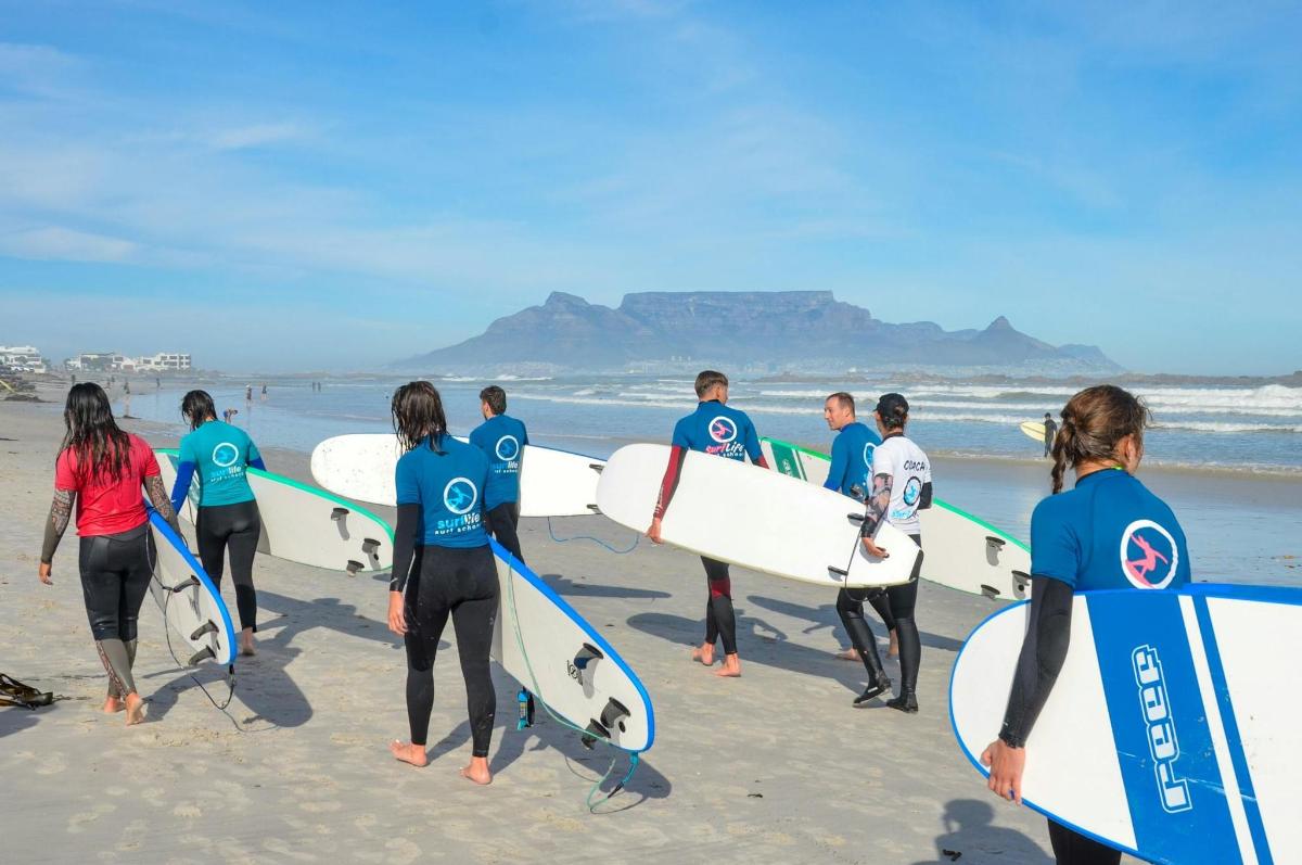en gruppe mennesker som går på stranden med surfebrett