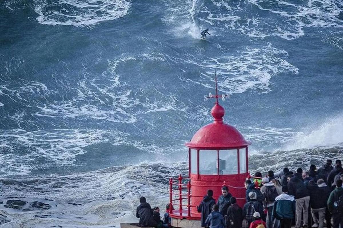 un grup de persones mirant un home fent surf a l'oceà