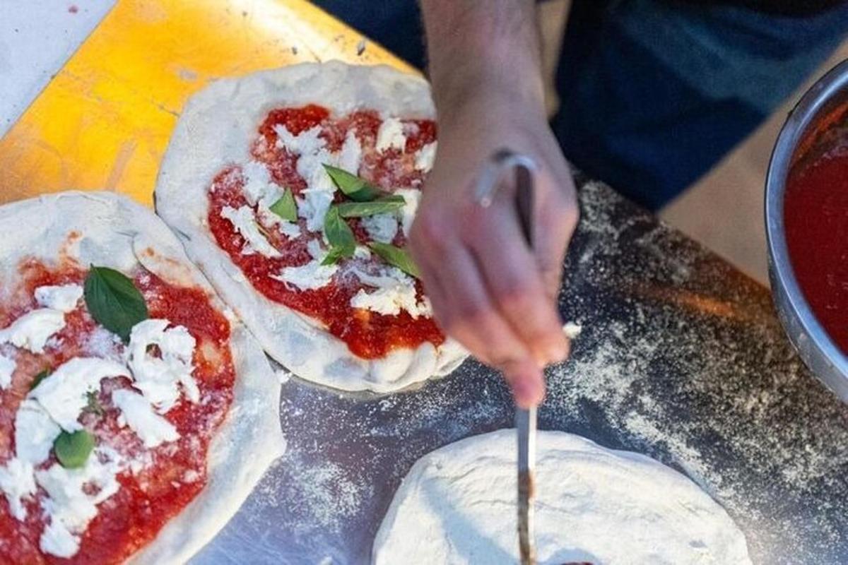Una persona agregando ingredientes a dos pizzas en una mesa.