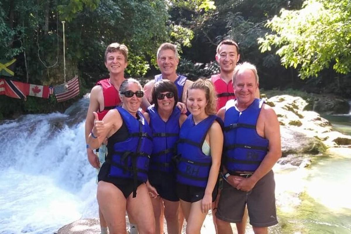 um grupo de pessoas usando coletes salva-vidas em pé em frente a uma cachoeira