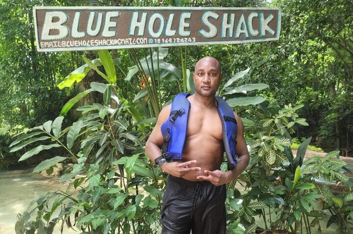 isang lalaking nakatayo sa harap ng isang sign na blue hole shack