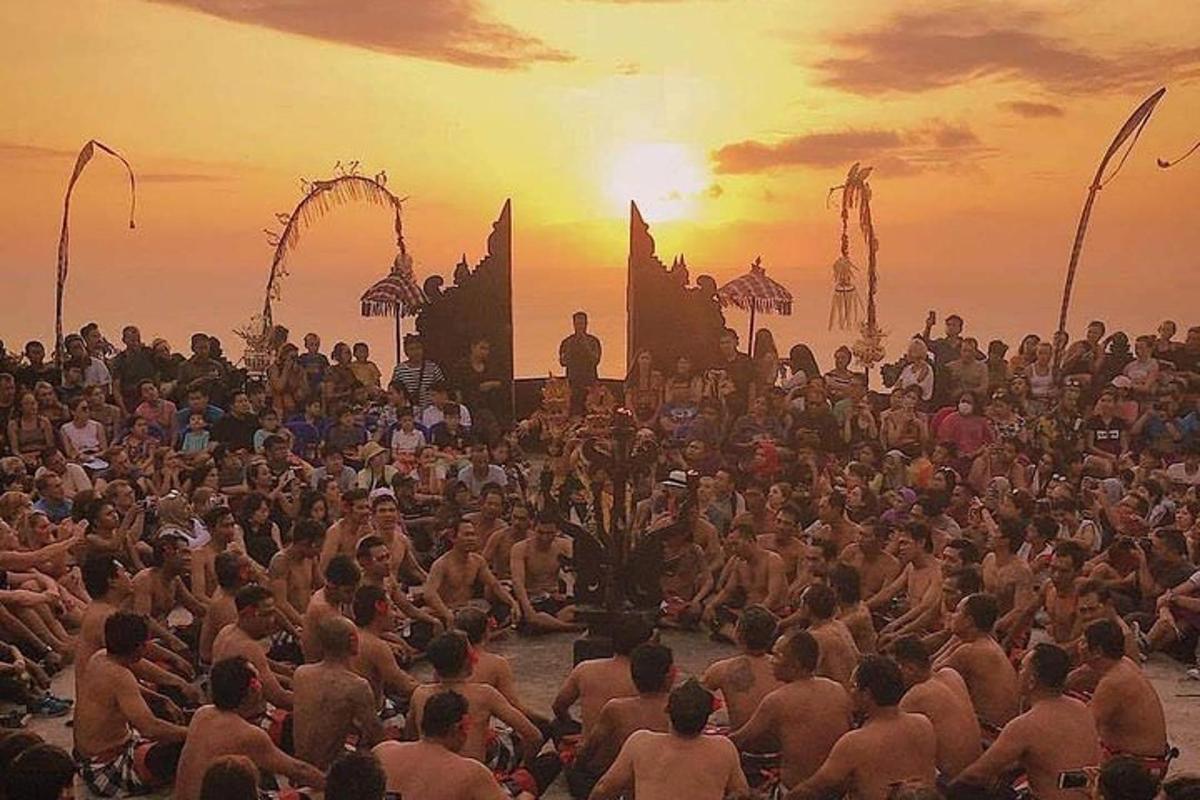 Un gran grupo de personas sentadas en la arena al atardecer.