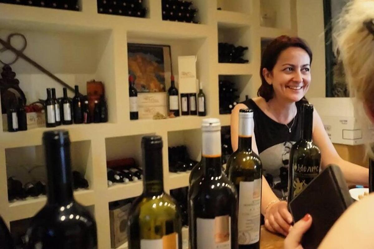 una dona dreta darrere d'un taulell amb un munt d'ampolles de vi