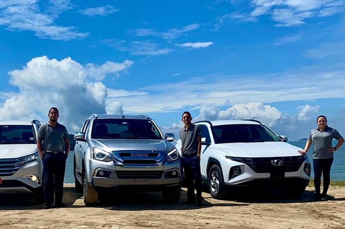 um grupo de pessoas em pé ao lado de carros em uma praia