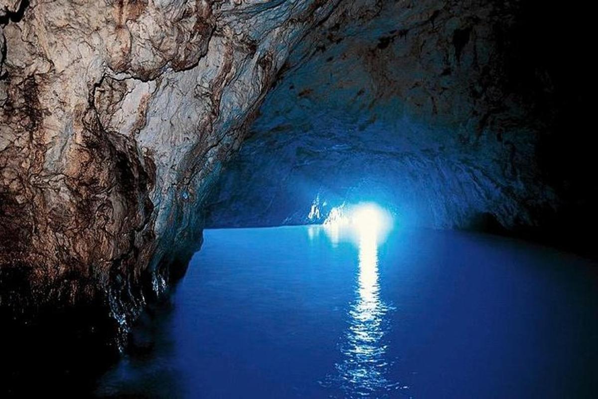 Una cueva oscura con agua azul y una persona dentro.