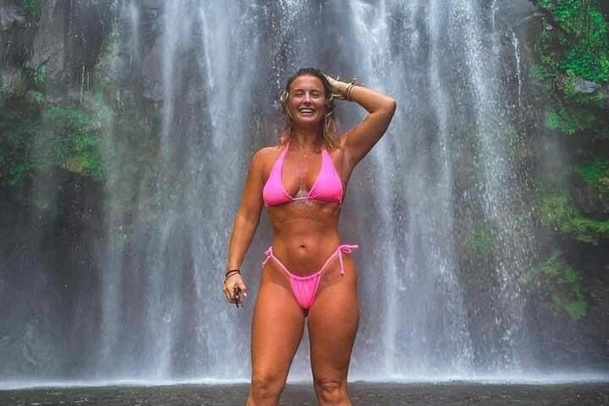 Kona í bleikum bikiní stendur fyrir framan foss