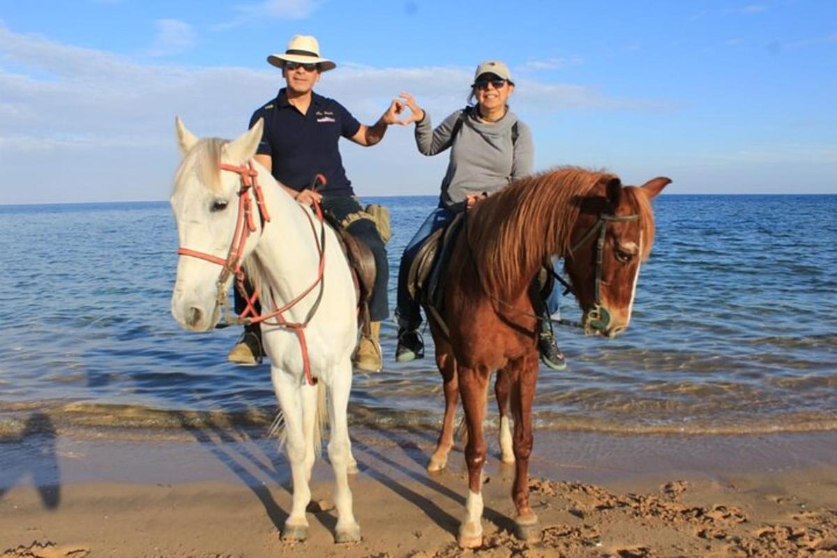en mann og en kvinne som rir på hester på stranden