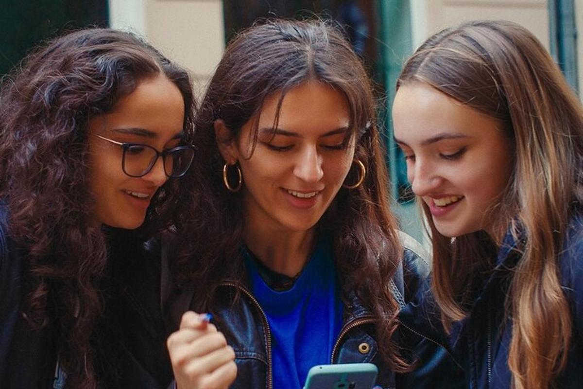 tři mladé dívky se dívají na mobilní telefon