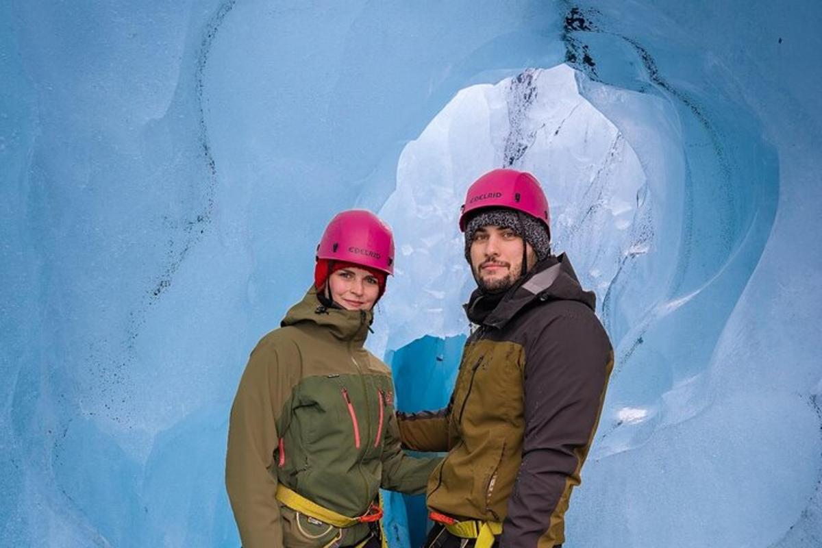 two people wearing helmets standing in front of an ice cave
