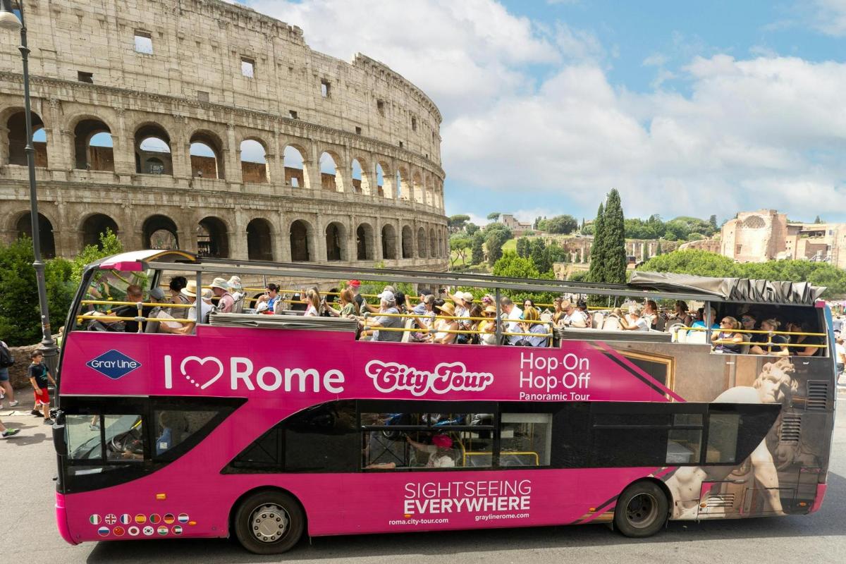 Un autobús rosa de dos pisos frente al coliseo.