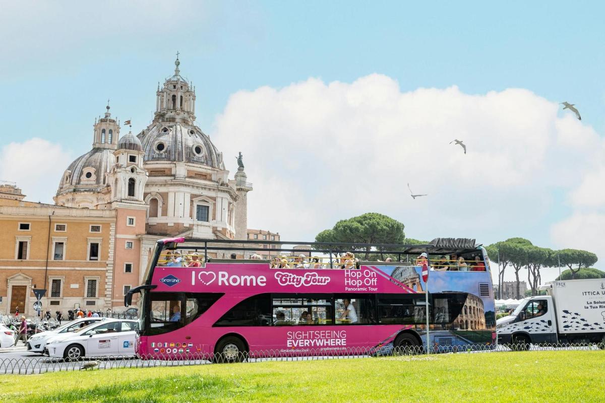 Un autobús rosa de dos pisos frente a un edificio.