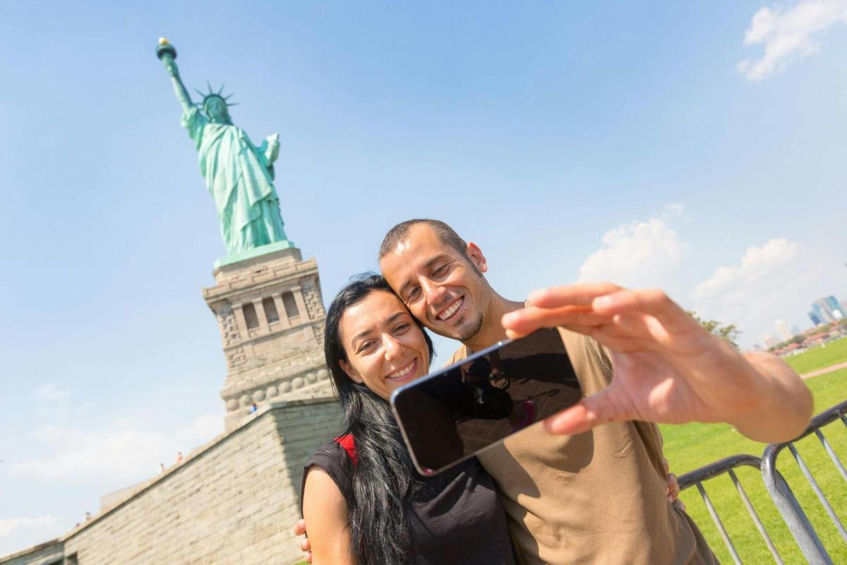 un homme et une femme prenant une photo devant la statue de la liberté