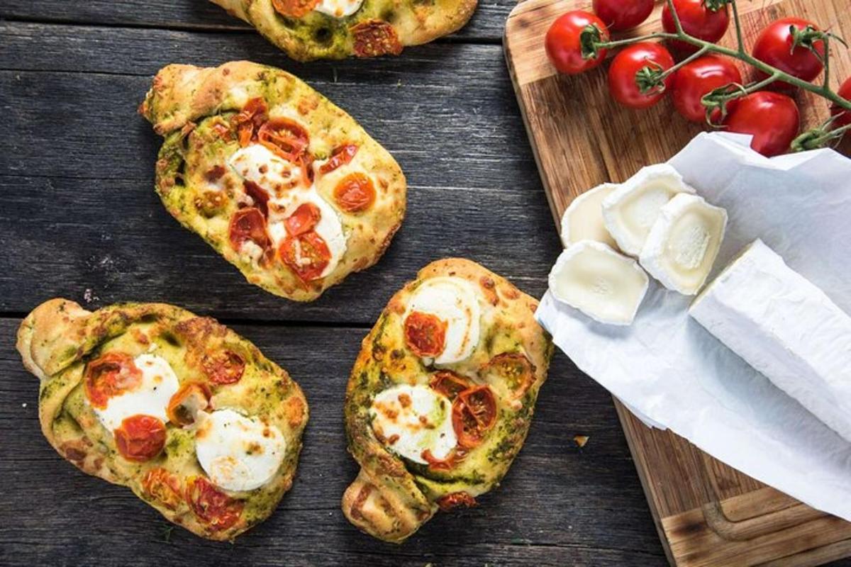 four small pizzas on a wooden cutting board with tomatoes
