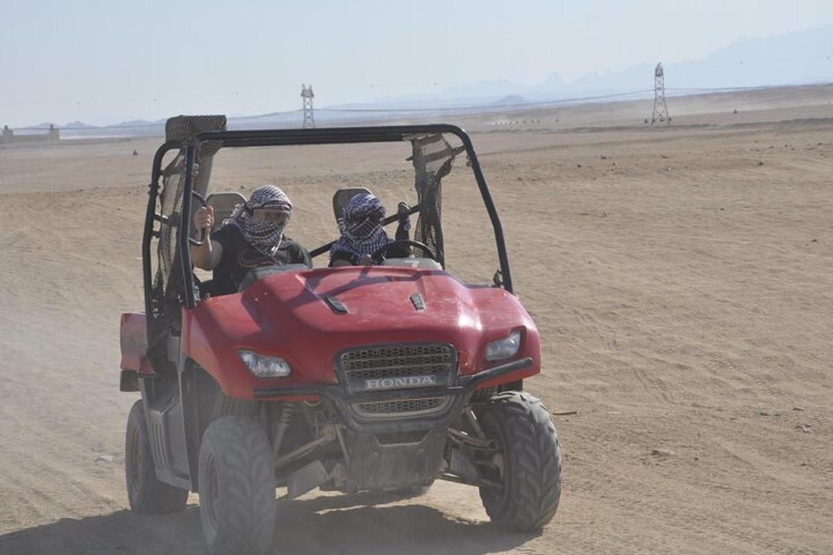 Dos personas viajando en un vehículo todo terreno rojo en el desierto.