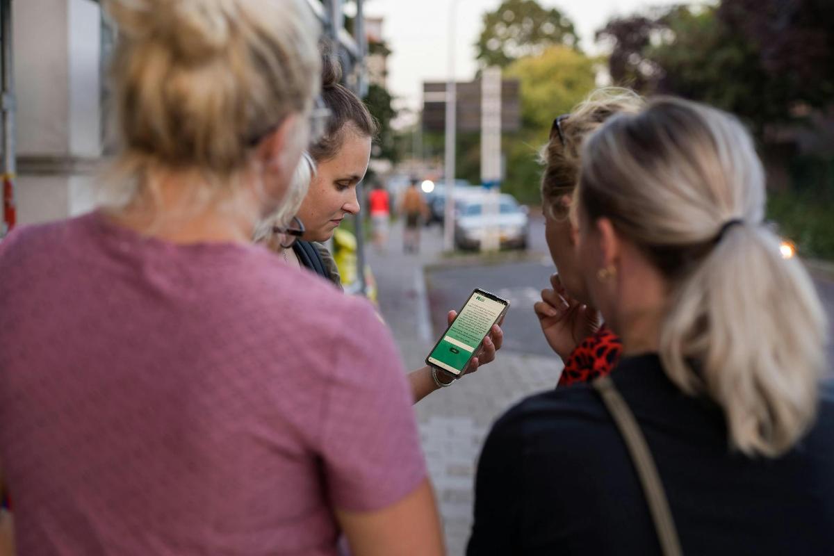 skupina žien kráčajúcich po ulici a pozerajúcich sa do mobilného telefónu