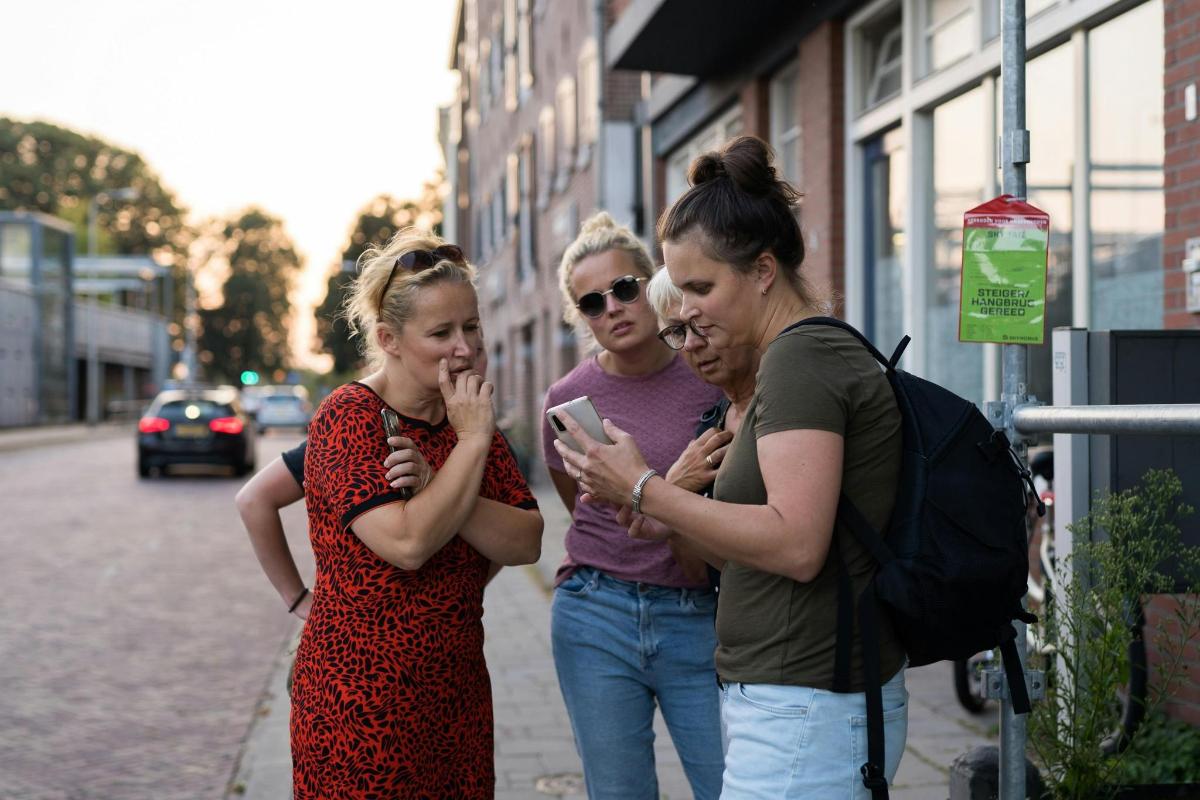 Tres mujeres paradas en una acera mirando un teléfono celular